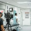 Cameraman capturing a scene in a hospital corridor with a professional video camera.