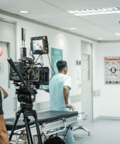 Cameraman capturing a scene in a hospital corridor with a professional video camera.