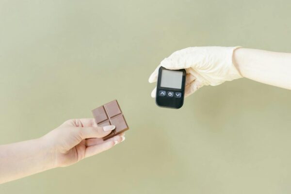 Close-up of hands holding a chocolate bar and glucose meter.