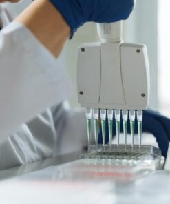 A scientist wearing a lab coat uses a multichannel pipette for liquid handling in a lab setting.