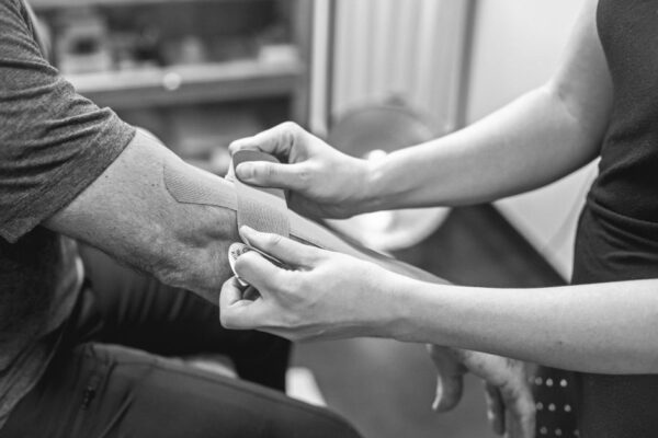 Close-up of kinesiology tape being applied on an elbow for therapeutic support in a healthcare setting.