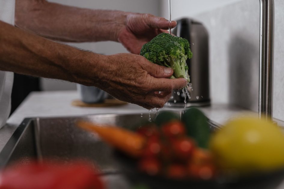 Suka Makan Sayur Buah Mentah? 7 Panduan Aman & Tips Cuci 1 Hands washing broccoli under running water in a kitchen sink, healthy cooking concept.