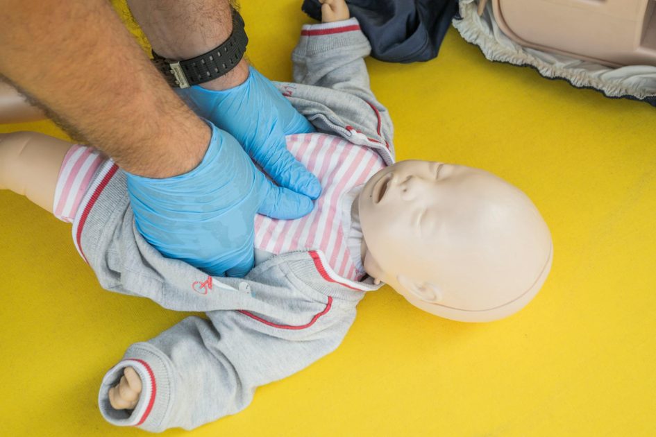 tas manikin CPR PRESTAN - SHOX ART Hands performing CPR on an infant mannequin for a first aid training session.