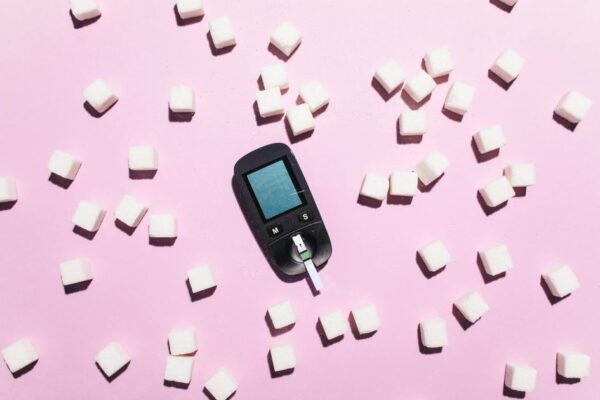 Blood glucose meter surrounded by sugar cubes on a pink background, highlighting diabetes awareness.