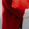 An elderly person in a red coat holds a cane, reflecting elegance and style.