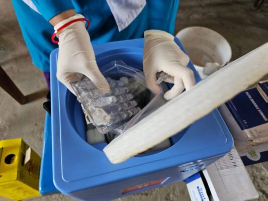 Healthcare worker using gloves handling medical vials in a laboratory setting.