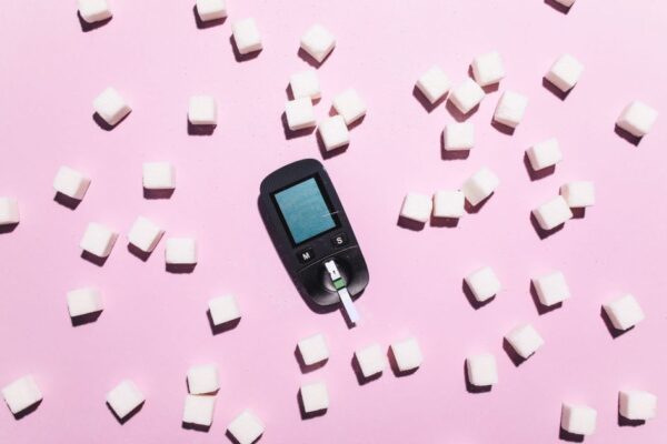 Blood glucose meter surrounded by sugar cubes on a pink background, highlighting diabetes awareness.