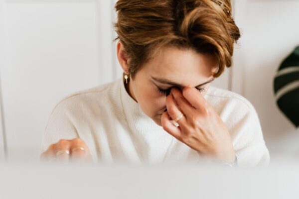 A close-up shot of a woman rubbing her eyes, conveying stress and fatigue indoors.