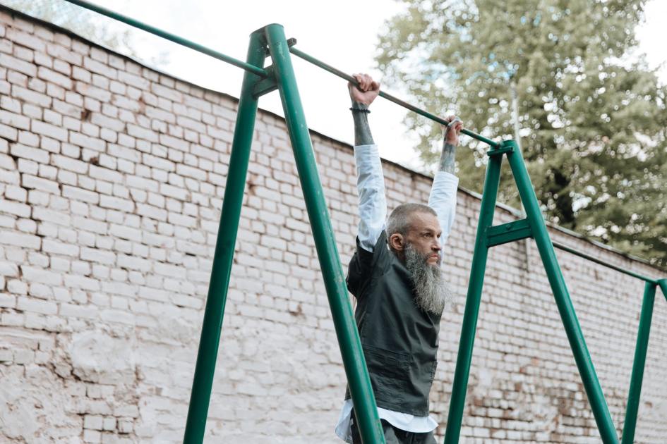 Durasi Dead Hang Ideal Sesuai Usia: Panduan Lengkap 2025 1 Bearded man exercising by hanging on monkey bars outdoors in a playground area.