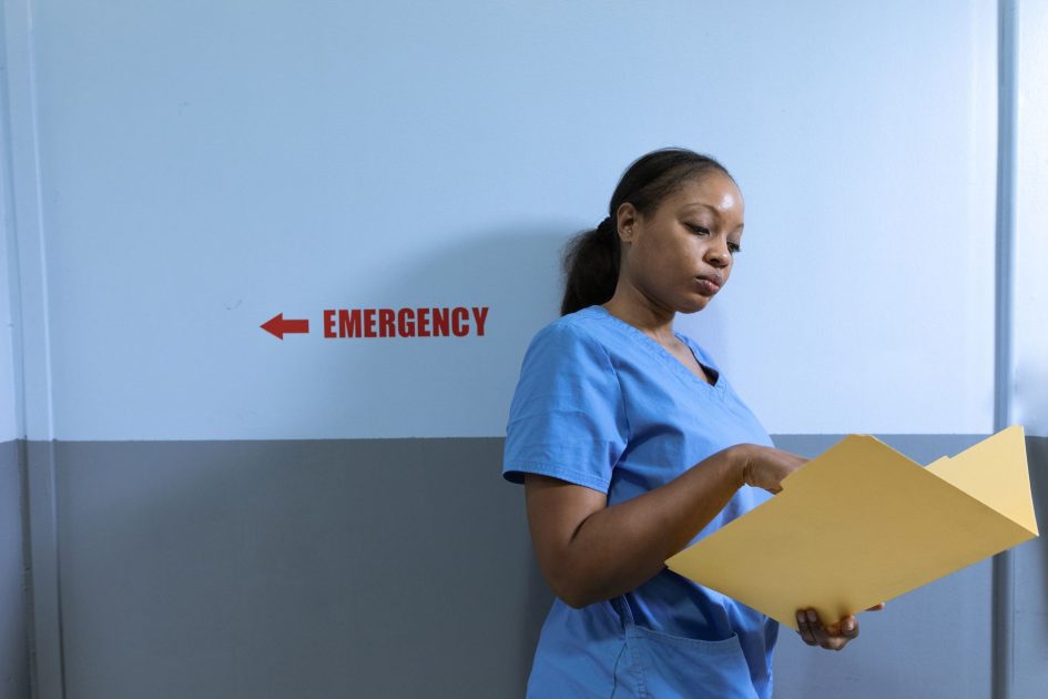 Reses RSUD Kuala Kurun Rayaniatie: 5 Standar Alat Kesehatan Prioritas 2024 1 A nurse in blue scrubs reads a folder near an emergency room sign in a hospital.