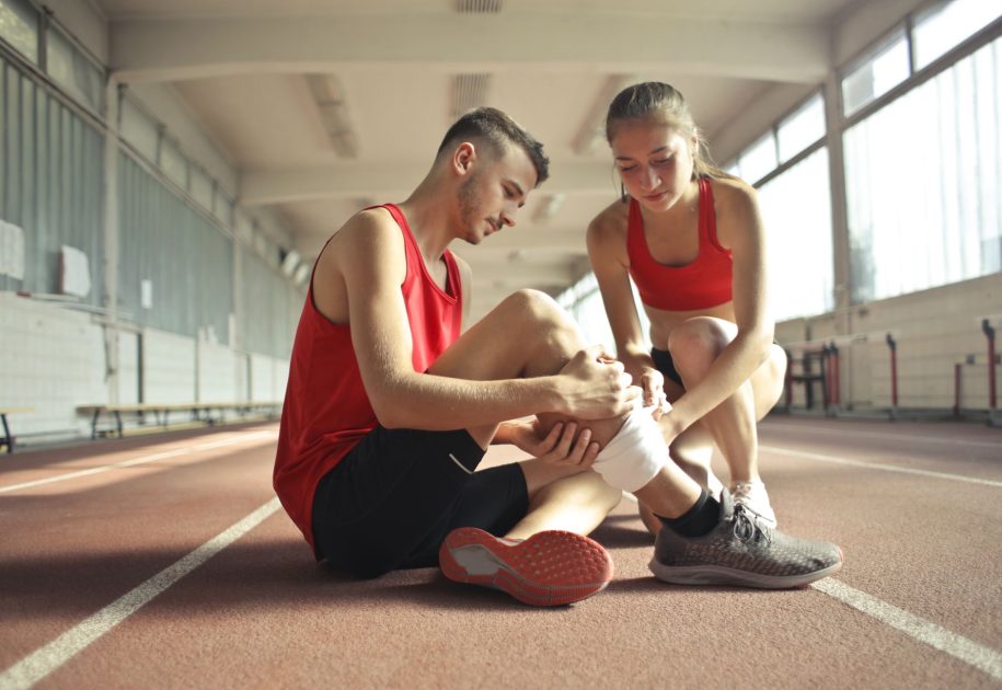 Rodri Bawa Timnas Spanyol Final: 5 Strategi Cedera & Pemulihan 1 Side view of athlete sitting on rubber track in sports hall while sportive female partner helping to band leg after injury