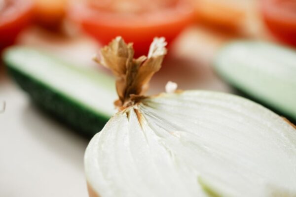A detailed close-up of a sliced onion with cucumbers and tomatoes in the soft focus background.