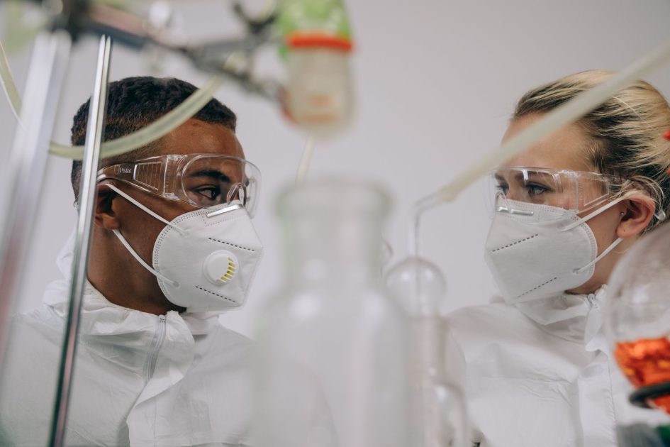 Checklist APD Laboratorium Clinik: Standar KEMENKES Terlengkap 2025 1 Two scientists in protective suits and masks working in a laboratory setting with equipment.