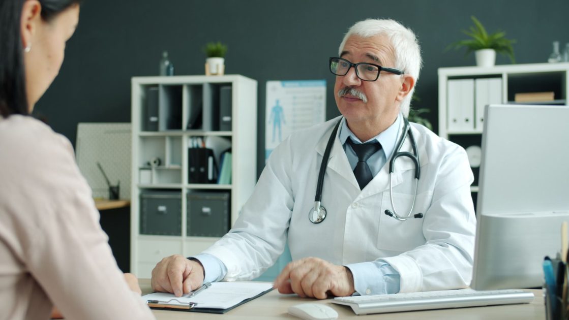 Senior doctor discussing health with patient in a modern medical office.