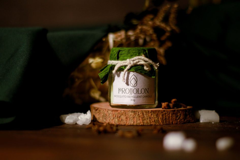A Projjolon mosquito repellent candle displayed on a wooden base, emphasizing eco-friendly and organic features.