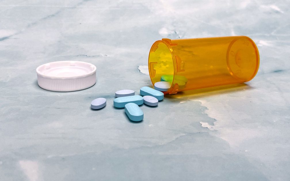 Bahaya Sabu Kokain Dipakai Pilot: 7 Risiko Kesehatan Kritis 1 Scattered blue pills and an orange prescription bottle on a light surface.