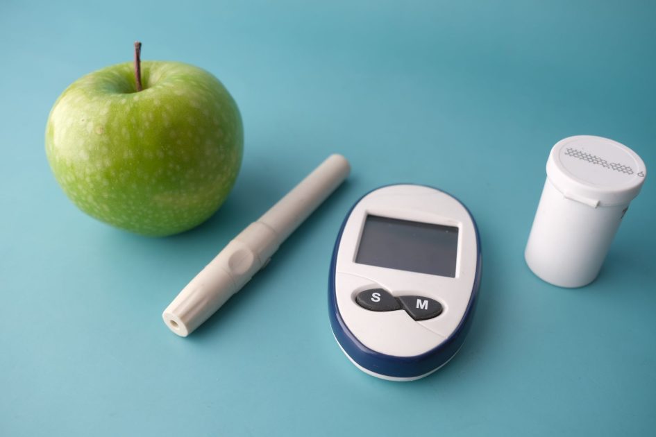 BGN Prioritaskan Aktivasi Dapur MBG: 7 Strategi Nutrisi 2024 1 Flat lay of a glucose monitor, apple, and insulin pen on a pastel background.