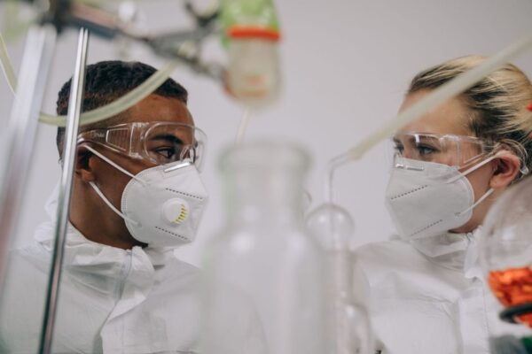 Two scientists in protective suits and masks working in a laboratory setting with equipment.