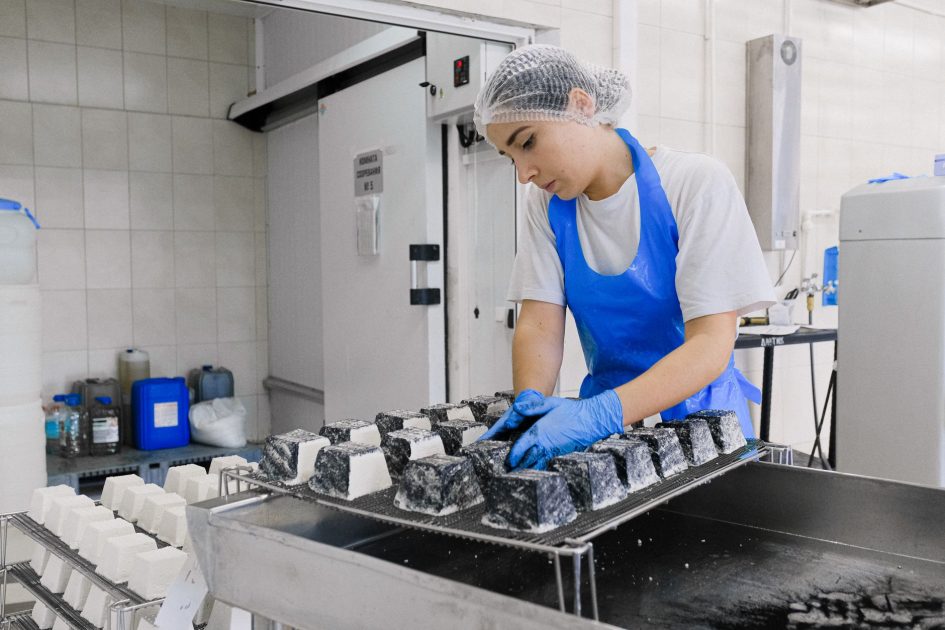 BPOM Kawal Keamanan Rendang 5 Ton: Panduan Lengkap 2025 1 A worker in a cheese factory examines cheese blocks during production, focusing on quality control.