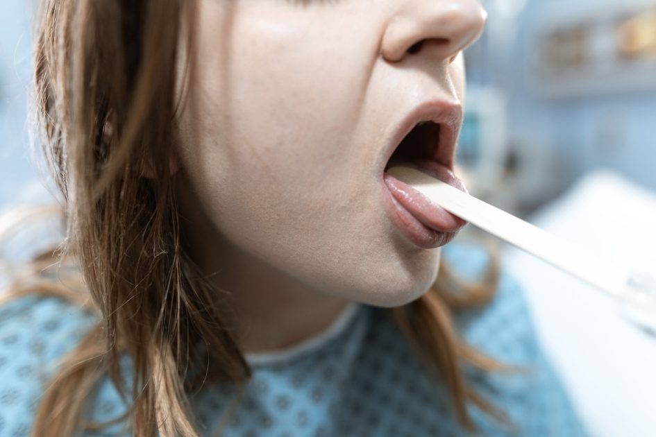 Cegukan Terus Menerus Jadi Tanda: 7 Kondisi Serius & Solusi Medis 1 Close-up of a woman having her throat examined in a medical setting with a tongue depressor.