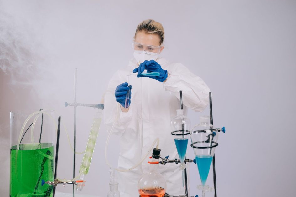 Erlab Captair vs Isolation Enclosure: Mana Pilihan Tepat? 2025 1 A scientist wearing protective gear performs an experiment with colorful chemicals in a laboratory.