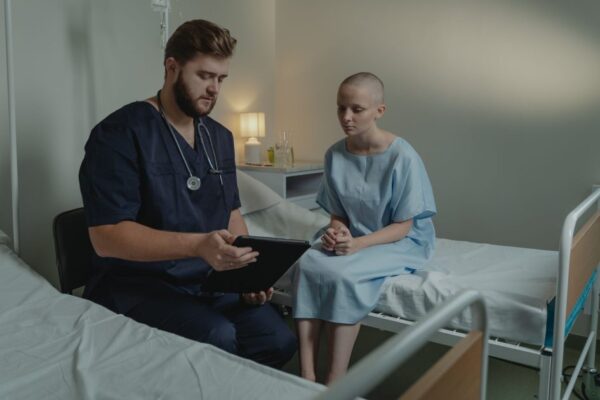 A doctor in a hospital ward consulting a patient with a digital tablet.