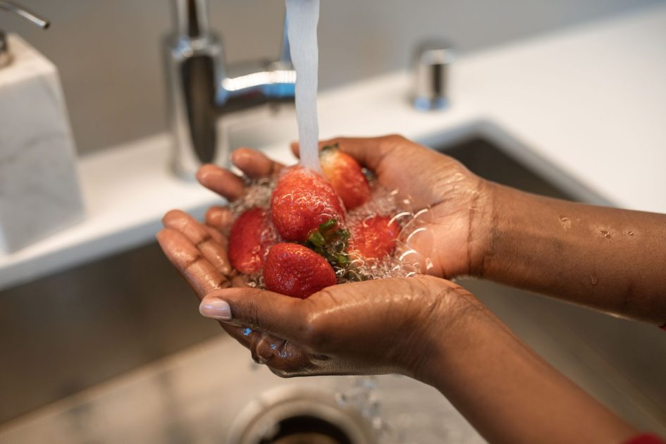Food Prep MPASI Simpel Bebas Bakteri: Panduan 10 Langkah Praktis 1 Close-up of hands washing strawberries under running water in a kitchen sink, focusing on freshness and cleanliness.