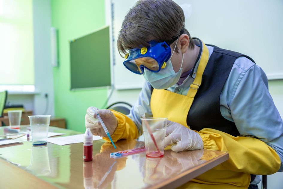 Student in lab attire performing a chemistry experiment with safety gear.
