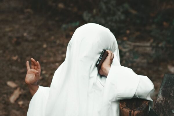 Person in ghost costume using smartphone outdoors. Perfect for Halloween-themed content.