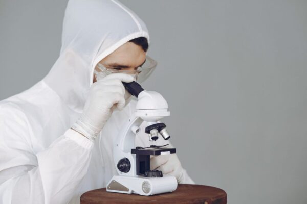 Scientist in protective gear using a microscope, focused on research and analysis.