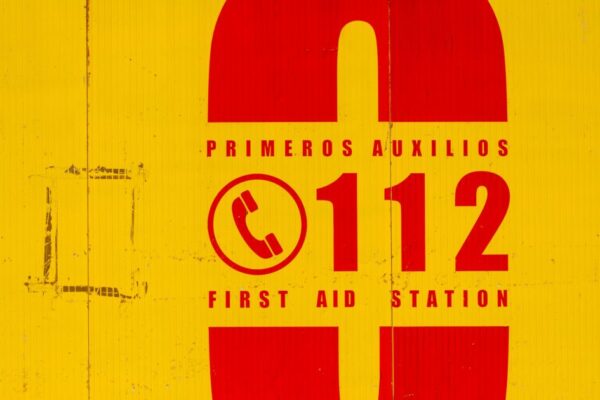 Bright yellow and red emergency sign indicating first aid station. Call 112 for emergencies.