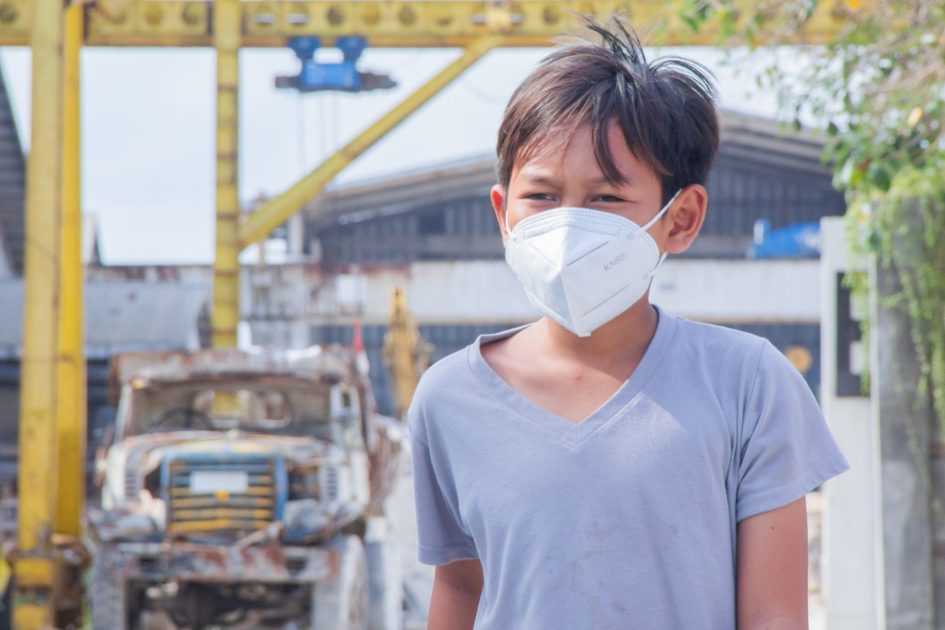 Infografis Kualitas Udara Wilayah Terdampak: 7 Data Penting 1 A young boy wearing a face mask stands in an industrial setting, highlighting safety during the pandemic.