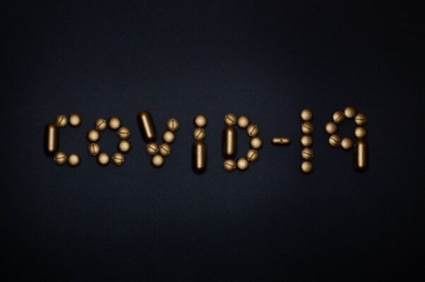Artistic representation of COVID-19 using golden pills on a black background, symbolizing healthcare and treatments.