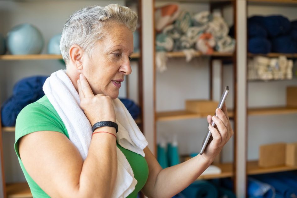 Kakek 63 Tahun Tangsel Rutin Lari: 7 Panduan Kesehatan Optimal 1 A senior woman using a smartphone to monitor her pulse after exercise in a gym setting.