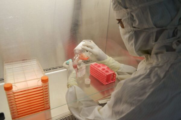 Scientist in protective clothing pouring liquid in a laboratory environment.