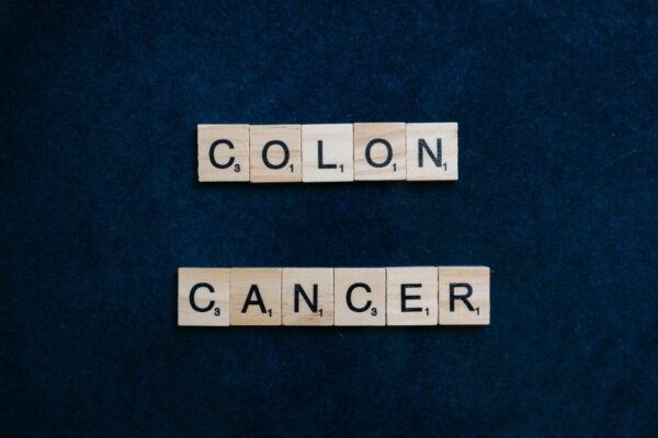 Wooden Scrabble tiles spelling 'Colon Cancer' on a blue background.