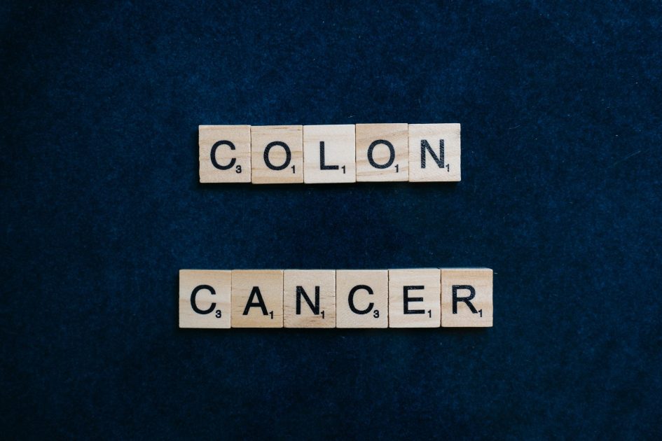 Wooden Scrabble tiles spelling 'Colon Cancer' on a blue background.