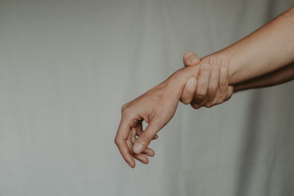 Unrecognizable male holding tight female wrist keeping close with force against white background