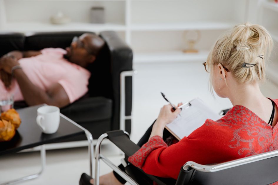Kemenkes Bakal Beri Layanan Kesehatan Mental: Panduan 7 Langkah 1 A professional therapist takes notes during a therapy session, engaging with a client.