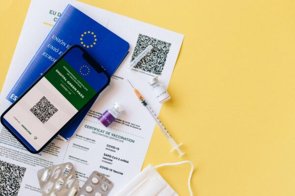 Digital vaccine passport and COVID-19 vaccination items including syringes and masks on a yellow background.