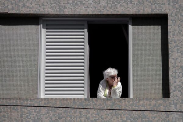 Senior woman looking out a window, contemplating the view from her apartment.
