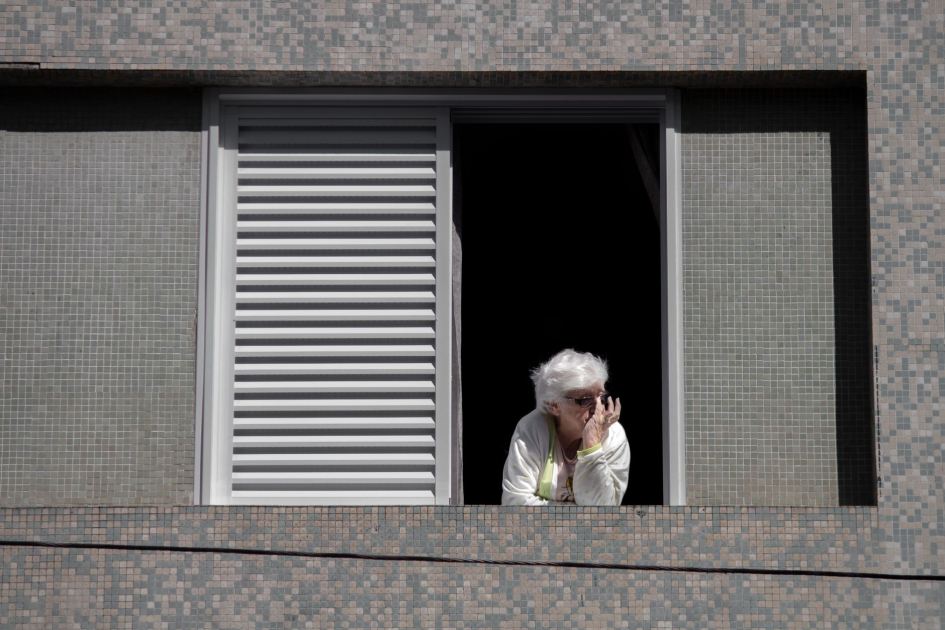 Kesepian Pengaruhi Otak: 4 Efeknya & Cara Mencegah 1 Senior woman looking out a window, contemplating the view from her apartment.