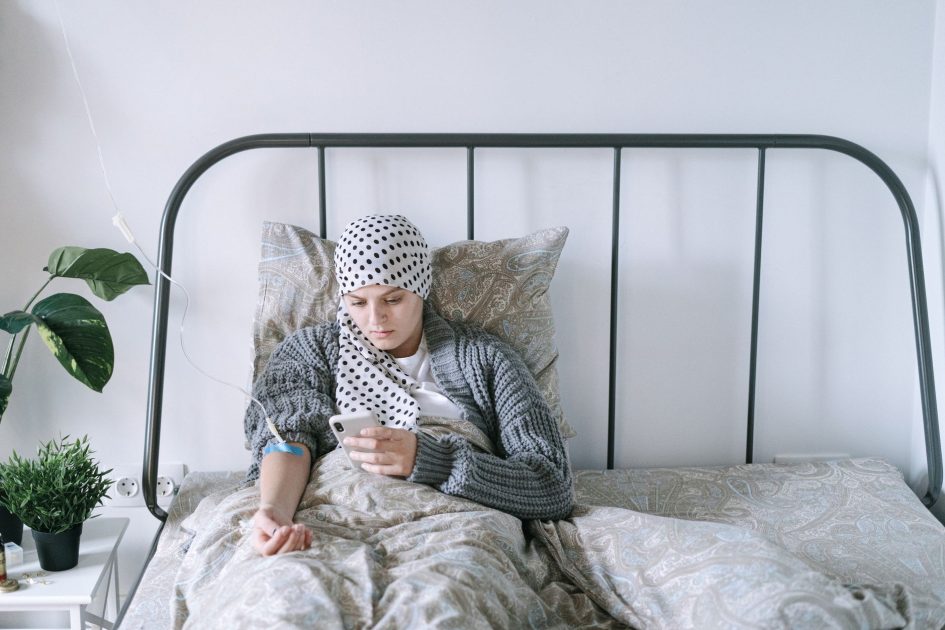 Kisah Survivor Kanker Limfoma Tangerang: 7 Inspirasi & Panduan Lengkap 1 A woman undergoing chemotherapy checks her smartphone in a hospital bed, symbolizing hope and recovery.