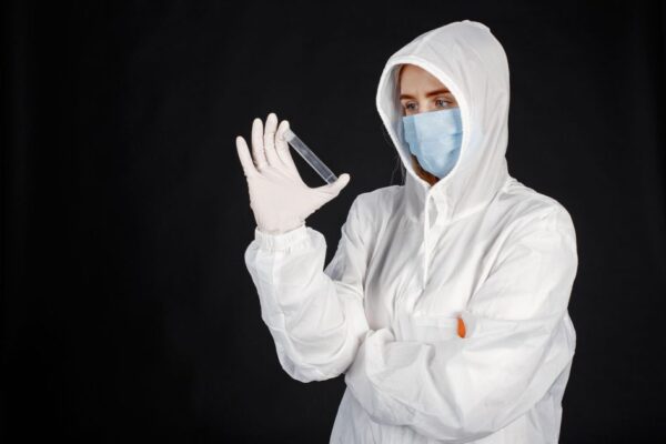 Scientist in full protective gear and mask analyzing a sample in a laboratory setting.