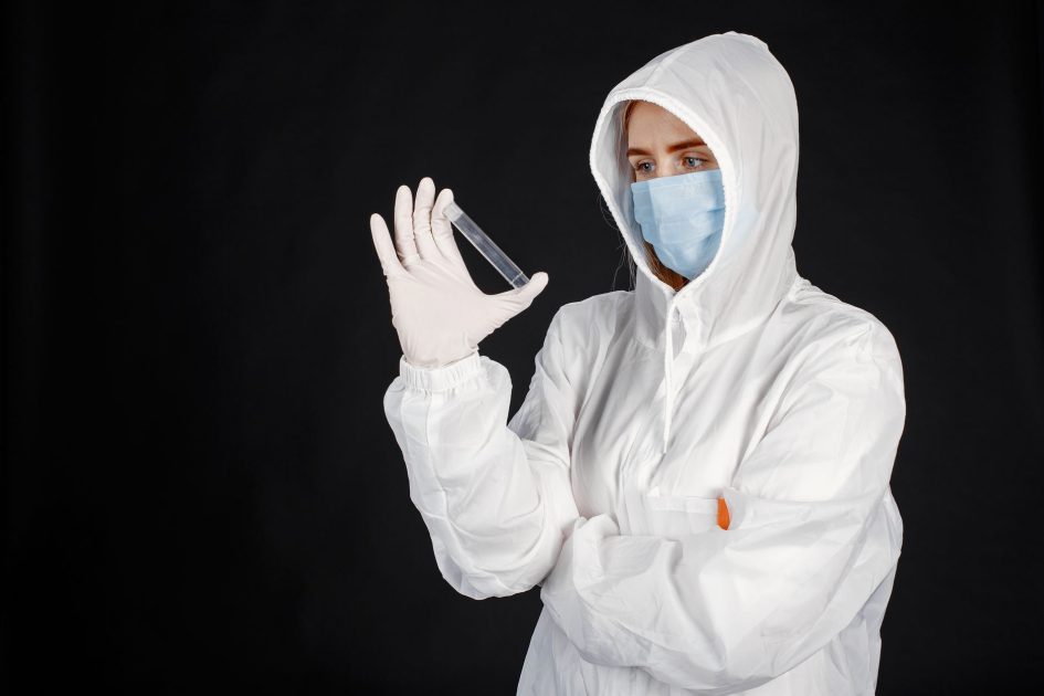 Scientist in full protective gear and mask analyzing a sample in a laboratory setting.