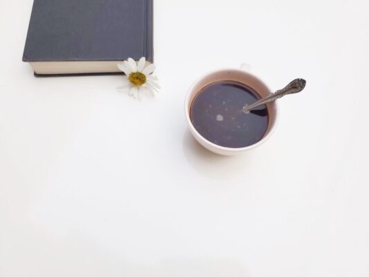 A serene scene of a coffee cup, book, and daisy on a white background.