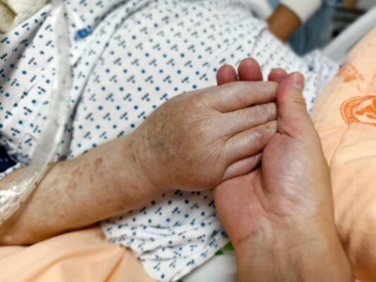 Close-up of hands holding in a hospital setting, symbolizing compassion and care.