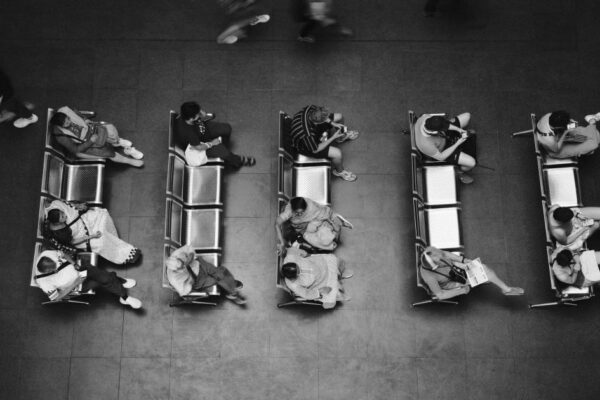 Black and white high angle photo of people sitting and waiting at a station.