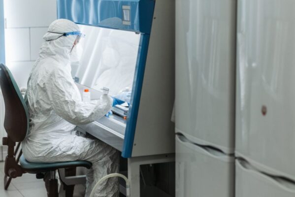 Scientist in protective gear working with laboratory equipment in a controlled environment.