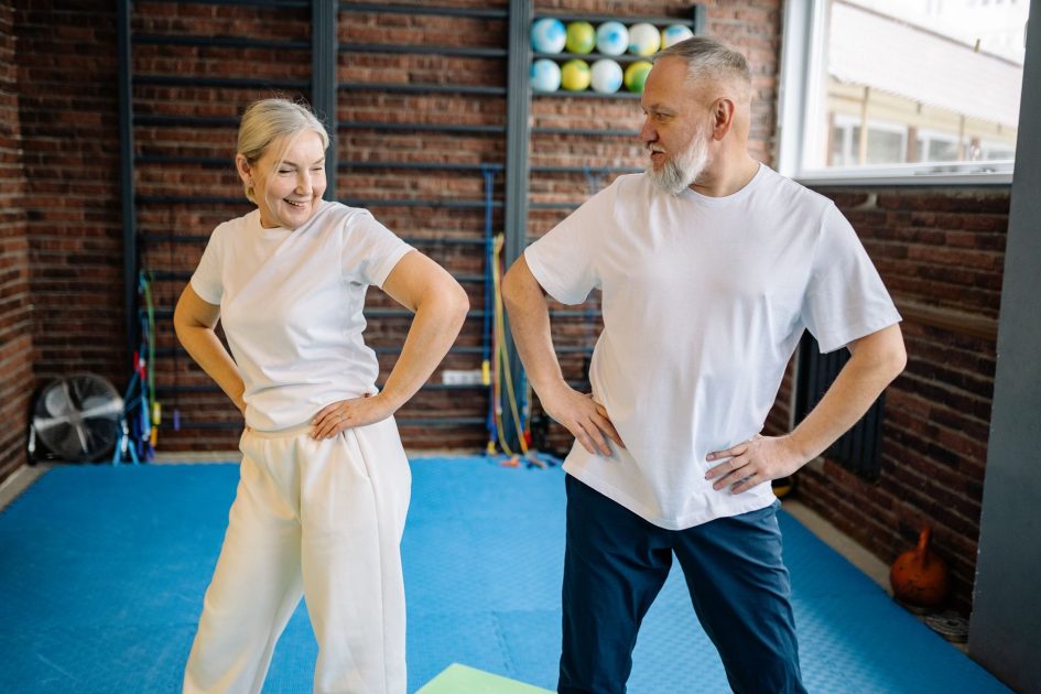 Rajin Olahraga Bantu Bikin Panjang Umur: Panduan 7 Langkah 1 Elderly couple in white shirts having fun exercising indoors for fitness and wellness.